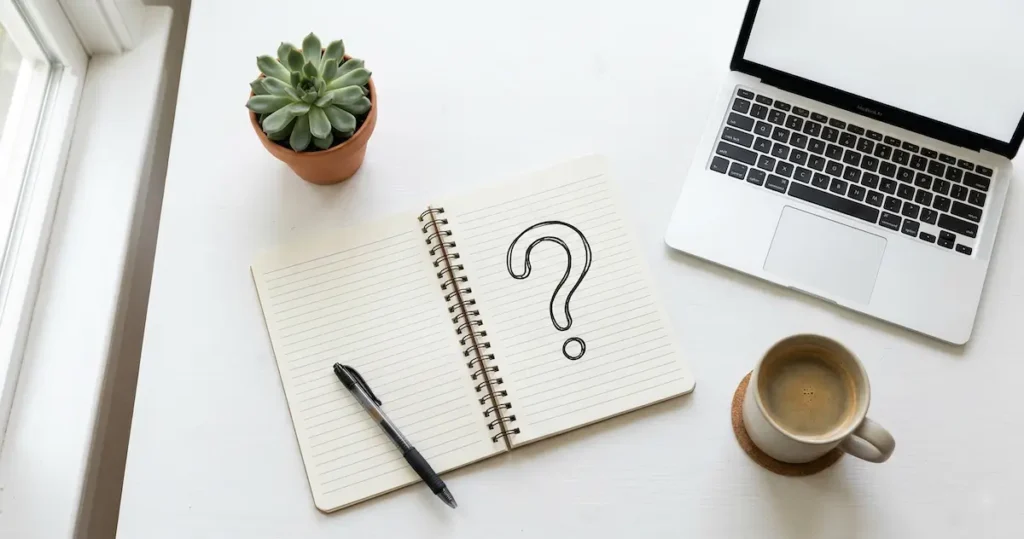 HeyGen AI Review: notebook with a hand-drawn question mark next to a laptop and coffee cup representing frequently asked questions